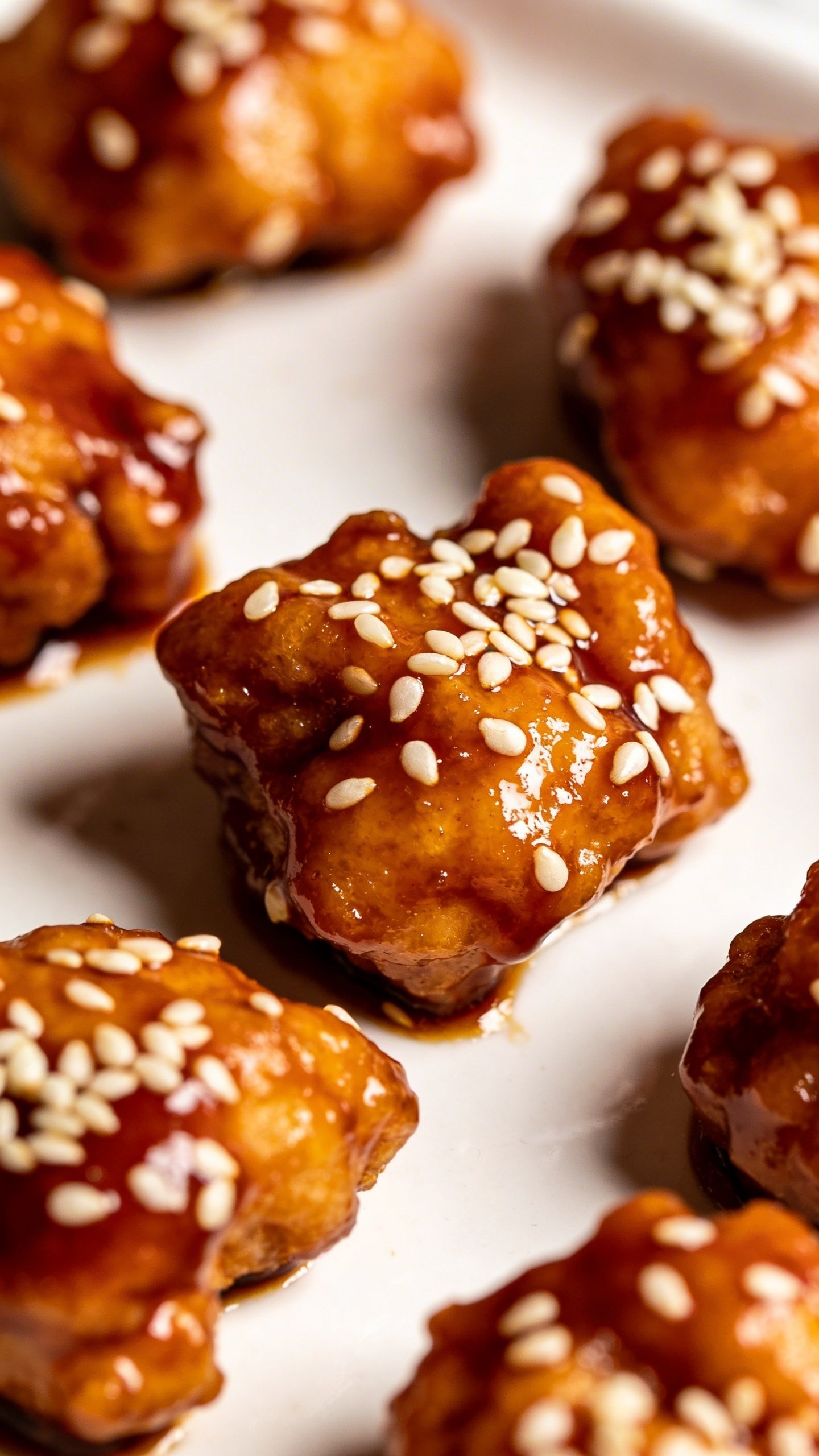Sticky Sesame Chicken: Glaze That Sticks Like Magic 3 Closeup of glossy sesame chicken bites on a white plate, dramatic shallow depth of field